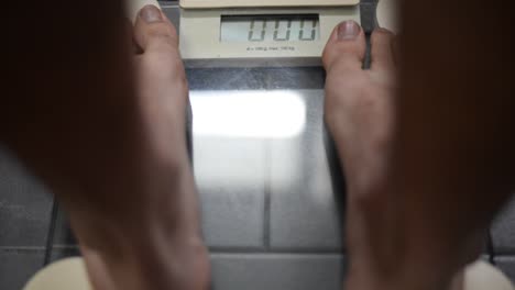 close up of feet stepping onto a digital bathroom scale on grey tiles