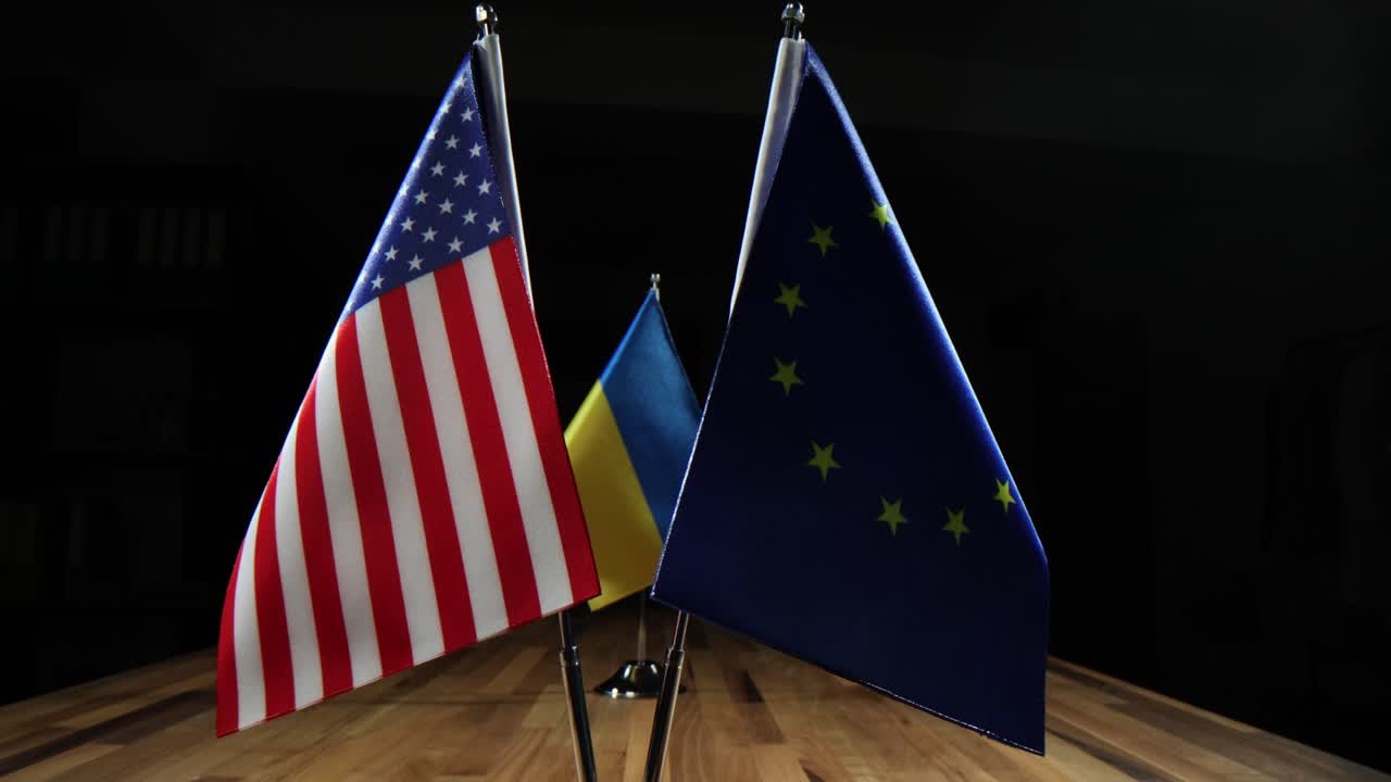 A small Ukrainian desk flag stands on a wooden surface against a dark background