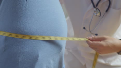 close up side view of male doctor's hands using tape measuring fat male patient's waist