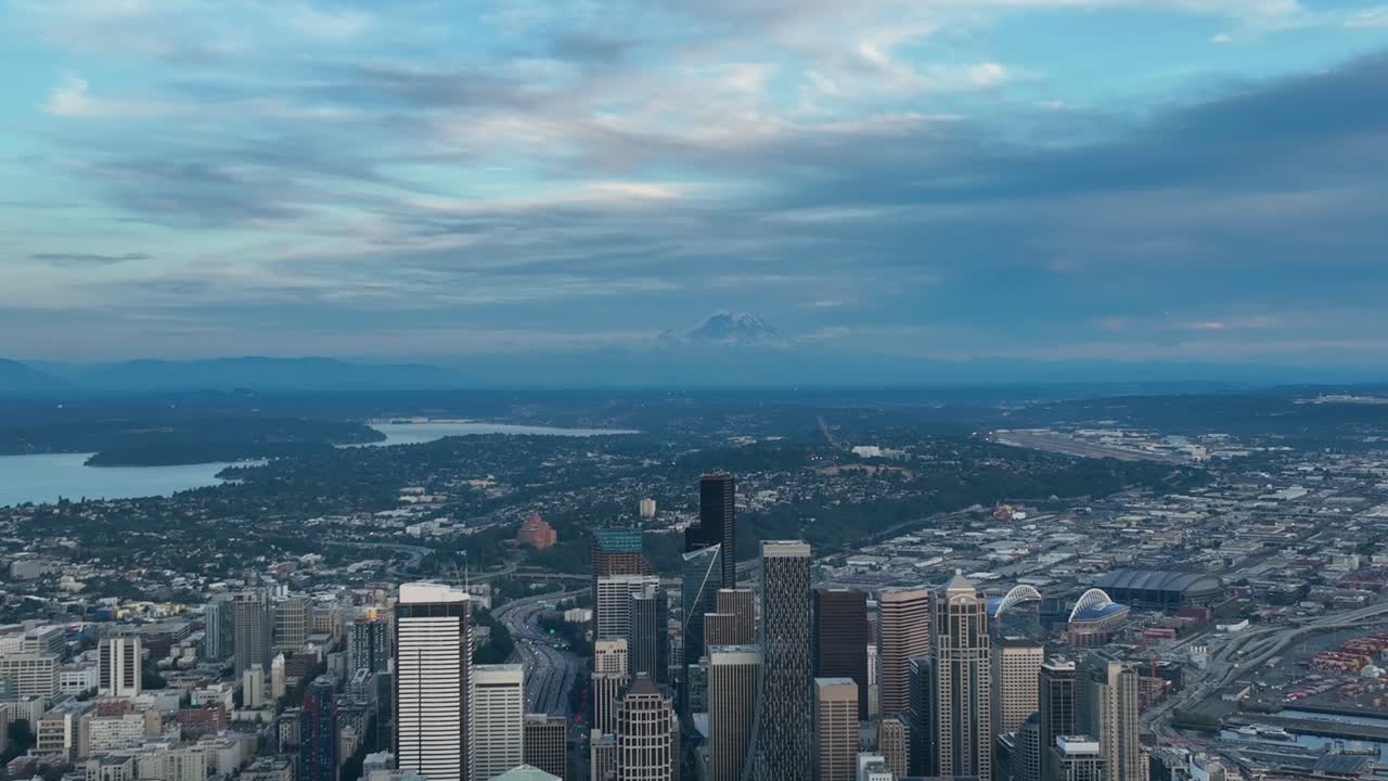 Wide aerial view of Seattle's skyscrapers reaching up to the clouds and Mount Rainier hidden in the distance