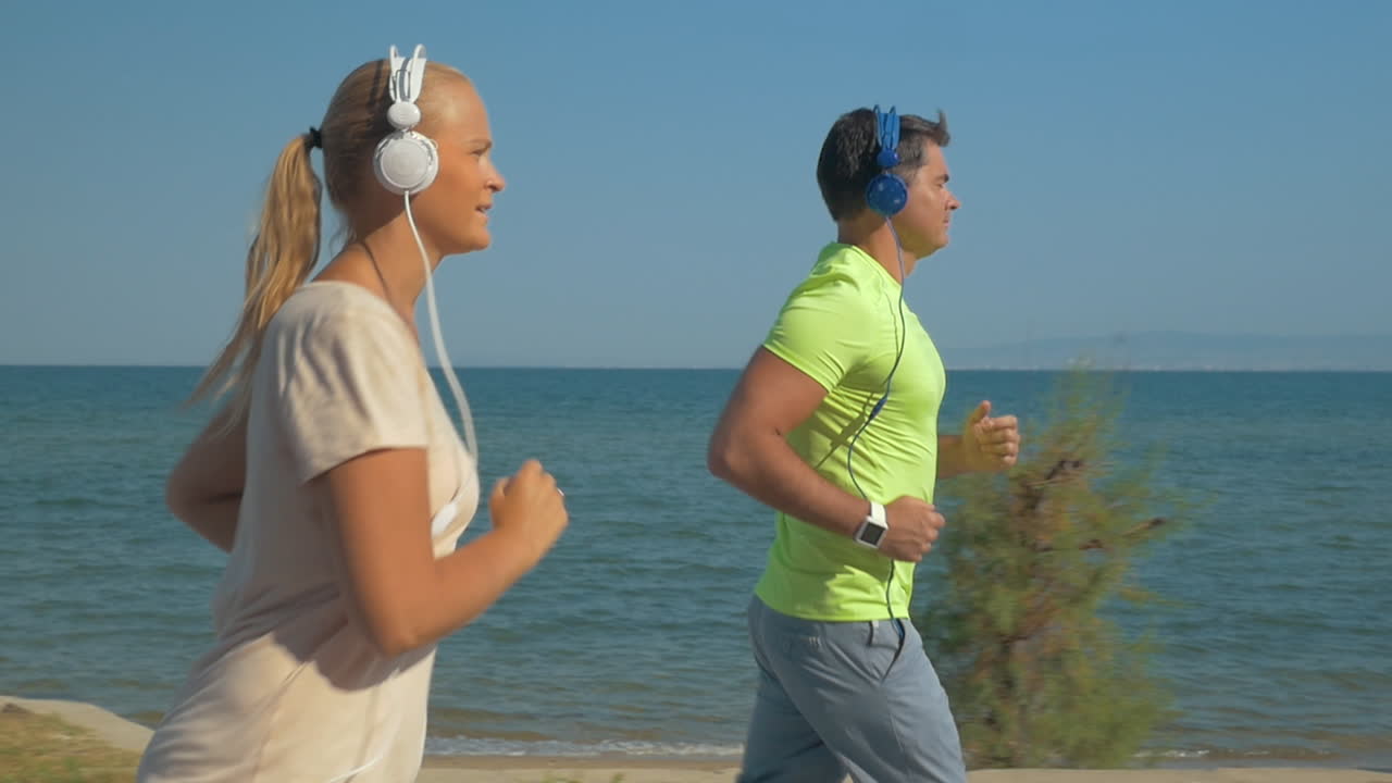 pareja con auriculares corriendo a lo largo del frente del mar