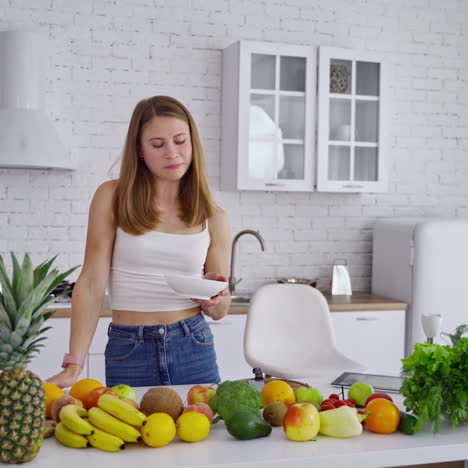 young woman in the modern kitchen. beautiful female is eating while standing at the table full of organic vitamins. healthy lifestyle. dieting concept.