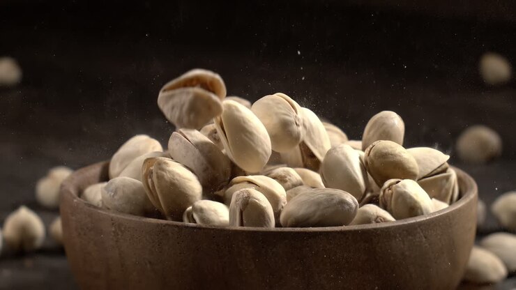 Wooden bowl filled with pistachios on dark wooden table, tasty salted nuts scattered around, healthy snack and natural food concept. Shot on super slow motion camera 1600 fps
