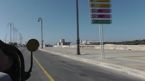 Sightseeing-from-inside-a-traditional-yellow-Cuban-Moto-Taxi-while-driving-along-the-famous-ocean-road-called-Malecon-in-Havana-on-a-sunny-day-passing-people-walking-on-the-sidewalk