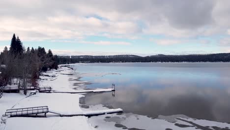 snowy icy frozen lake in winter with empty snow covered boat wharf jetty at lake front houses in mccall, idaho, usa - aerial drone slowly rising