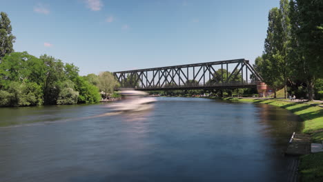 Timelapse-De-Barcos-Que-Viajan-Pasando-Por-Debajo-De-Un-Puente-Ferroviario-Con-Sendero-En-Caputh,-Schwielowsee,-Distrito-De-Potsdam-mittelmark,-Brandeburgo,-Alemania