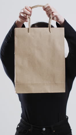 vertical video of caucasian woman holding paper shopping bag with copy space on white background
