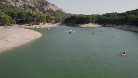 Vista-Aérea-Del-Lago-El-Chorro-De-Málaga,-Rodeado-De-Pinos,-Con-Turistas-Disfrutando-De-Paseos-En-Bote-Y-Deportes-Acuáticos