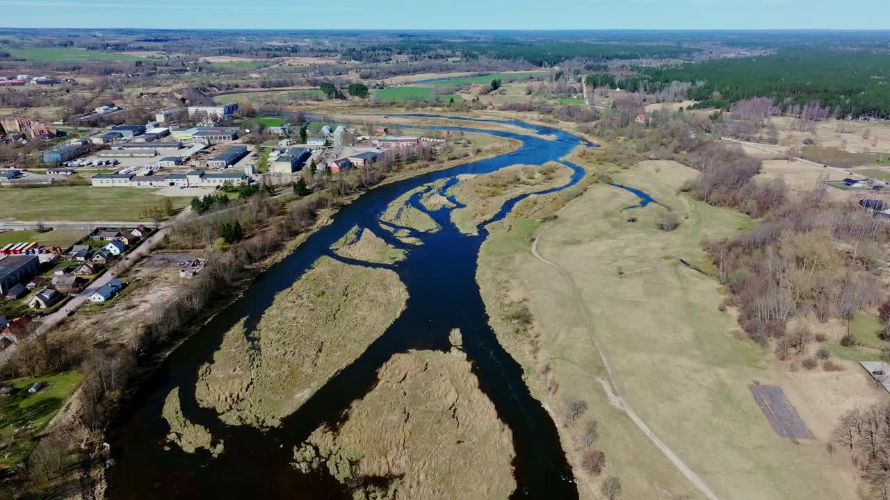 Venta river snakes through open landscape beside town of Kuldīga on clear day