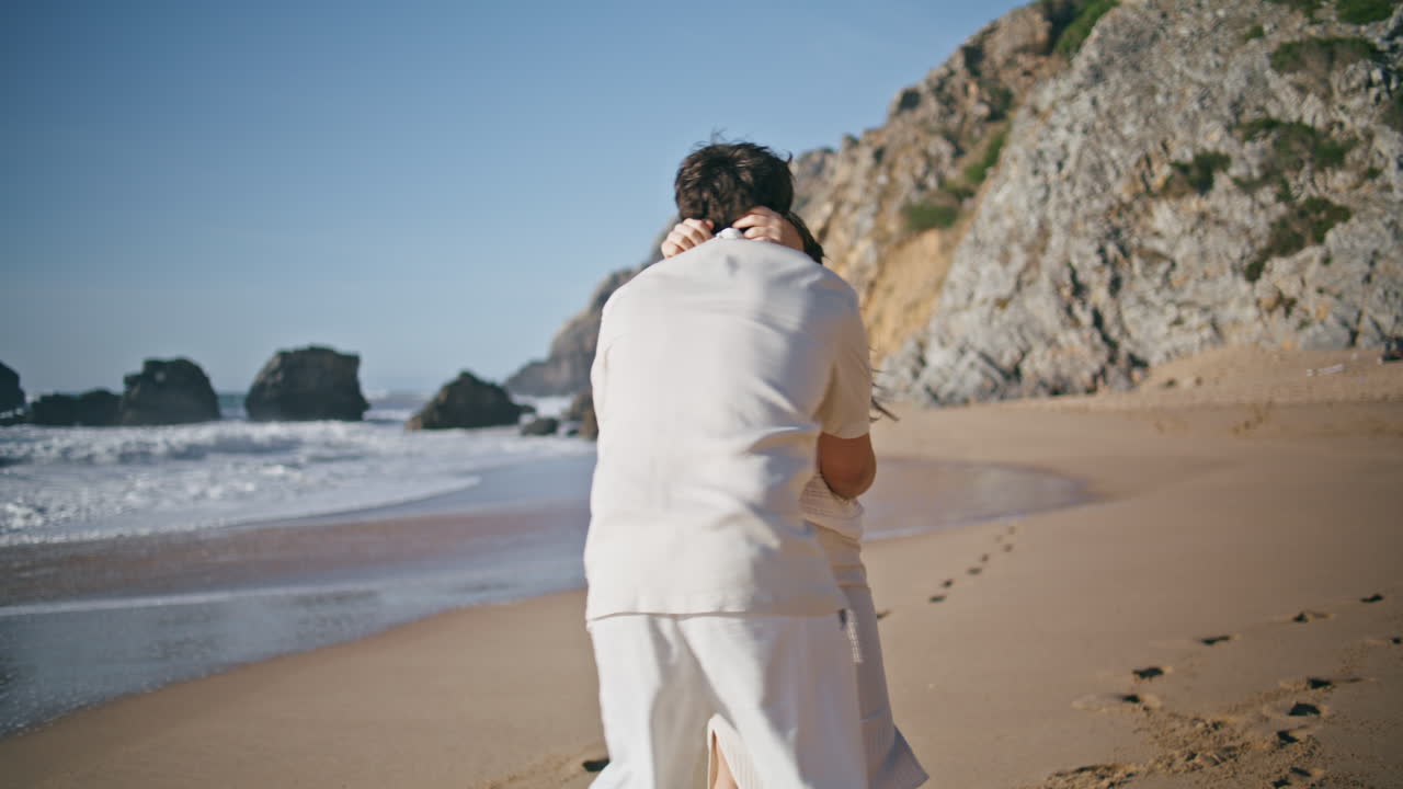 행복한 미래의 부모님이 모래 해변에서 키스하고 가까이서 회전합니다. 임신한 배우자