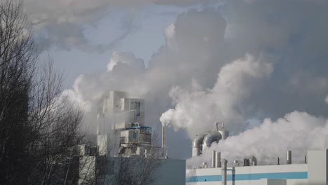 chimney stacks of paper mill releasing thick smoke at daytime in windsor, quebec, canada