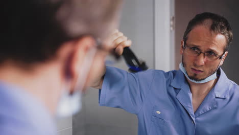 confused doctor in uniform cuts hair on head with trimmer