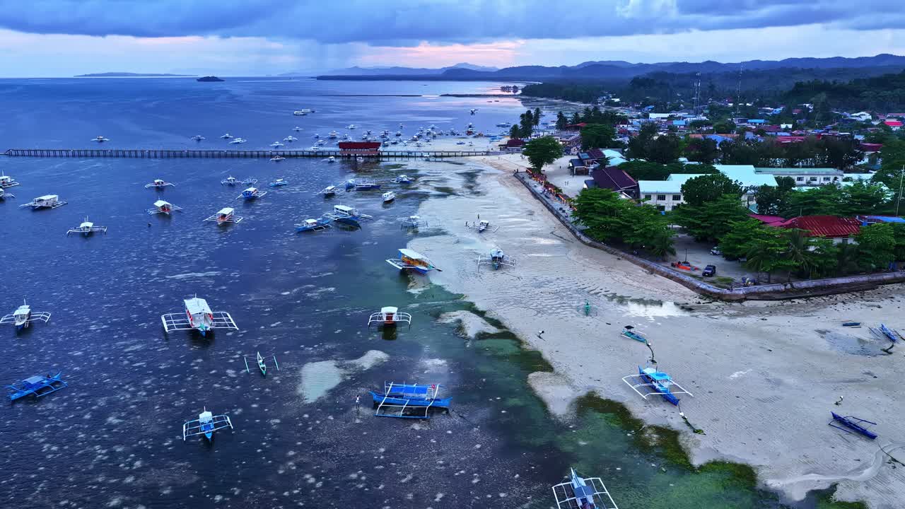 フィリピン、シアルガオ島、ジェネラル・ルナ、ポブラシオンVプロックVの砂浜の海岸線沿いの浅い青い水面にボートが点在するドローン空撮。