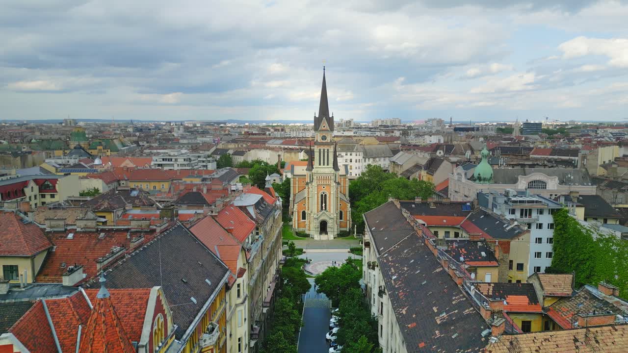 Ascending wide aerial shot of St. Francis of Assisi Parish, a historic Romanesque church framed by green trees and the city of Budapest, Hungary.