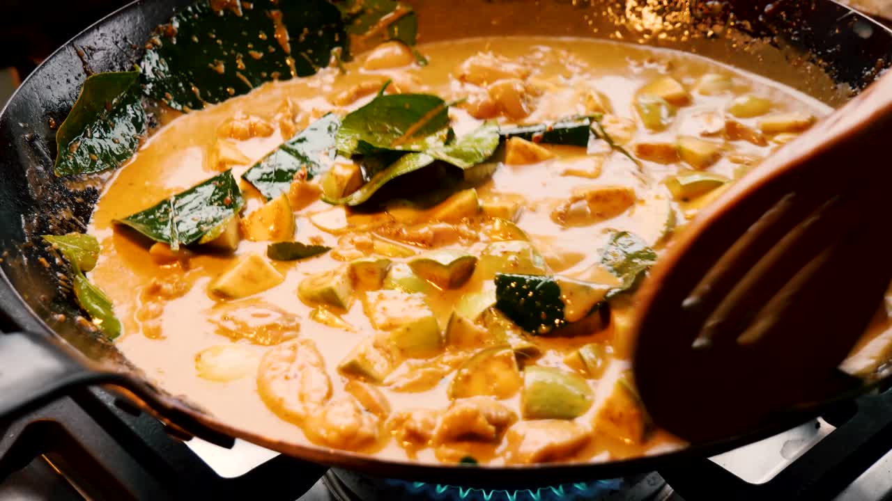 deliciosa comida tailandesa de verduras y curry de naranja se cocinan y se revuelven en un wok negro con una cuchara de madera enrejada, cierre estático