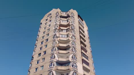 Footage-captures-the-ascent-on-a-high-rise-residential-concrete-Soviet-era-apartment-tower-block-against-a-blue-sky,-showcasing-its-utilitarian-design-and-historical-architecture