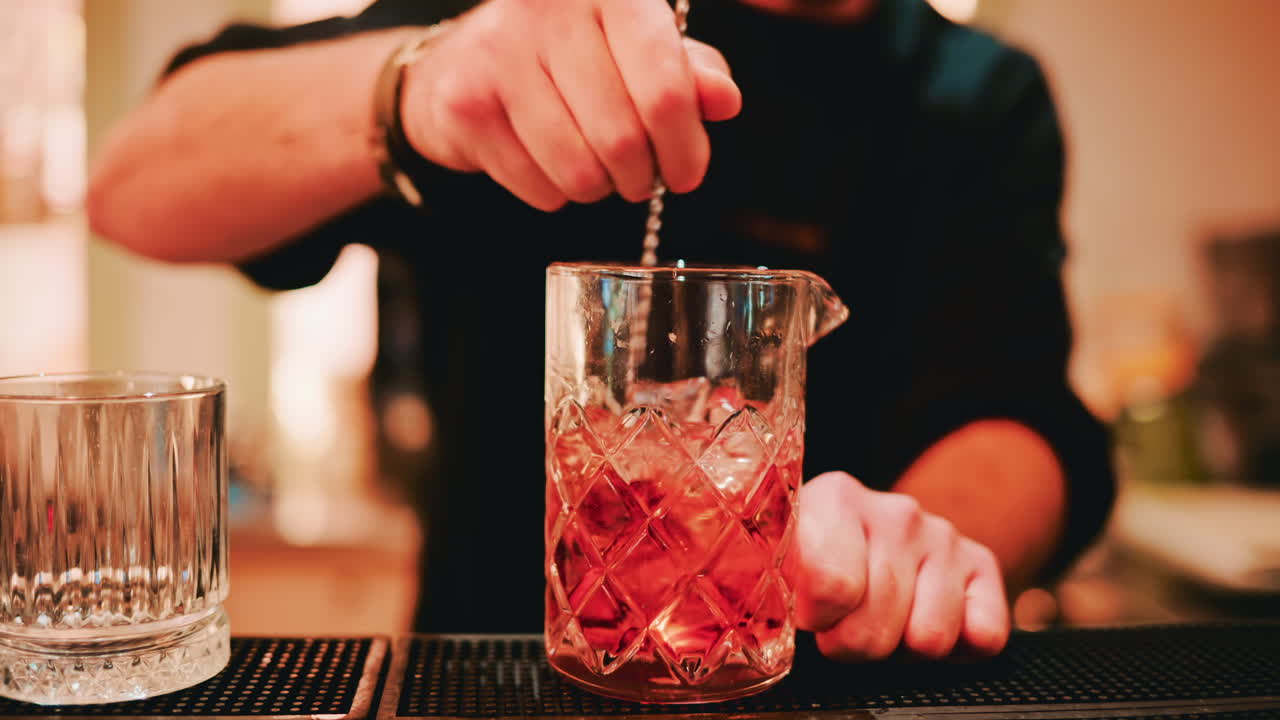 Close up shot of a bartender mixing a drink in a crystal mixing glass filled with ice