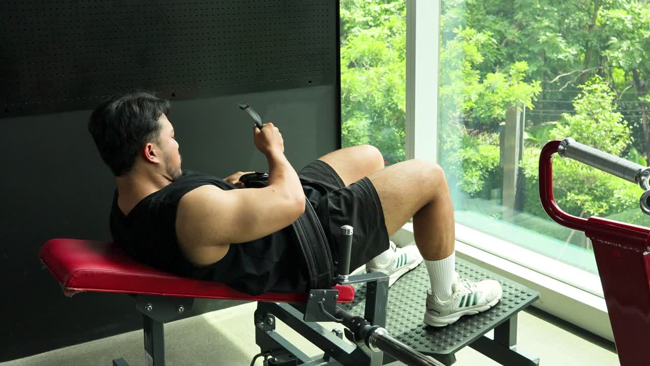 Athletic man on gym bench checks smartphone in bright, modern fitness center with natural light