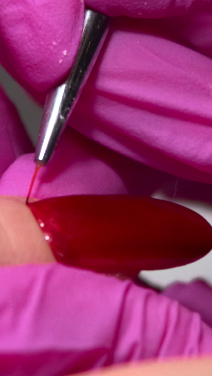 Close-up of Hand in Pink Gloves Applying Red Nail Polish