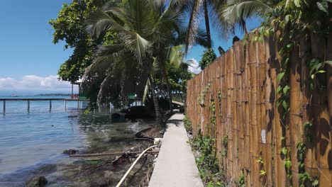 Point-of-view-walking-along-a-coastal-path-beside-a-fence-on-Bastimentos-Island,-Panama