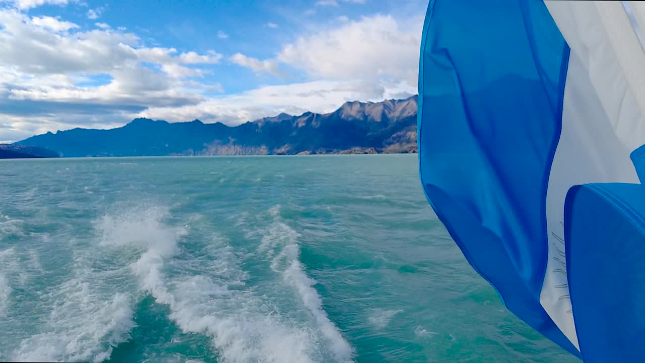majestuosa toma desde un barco de bandera argentina magistralmente fusionada con un lago turquesa, cielo azul e impresionantes montañas