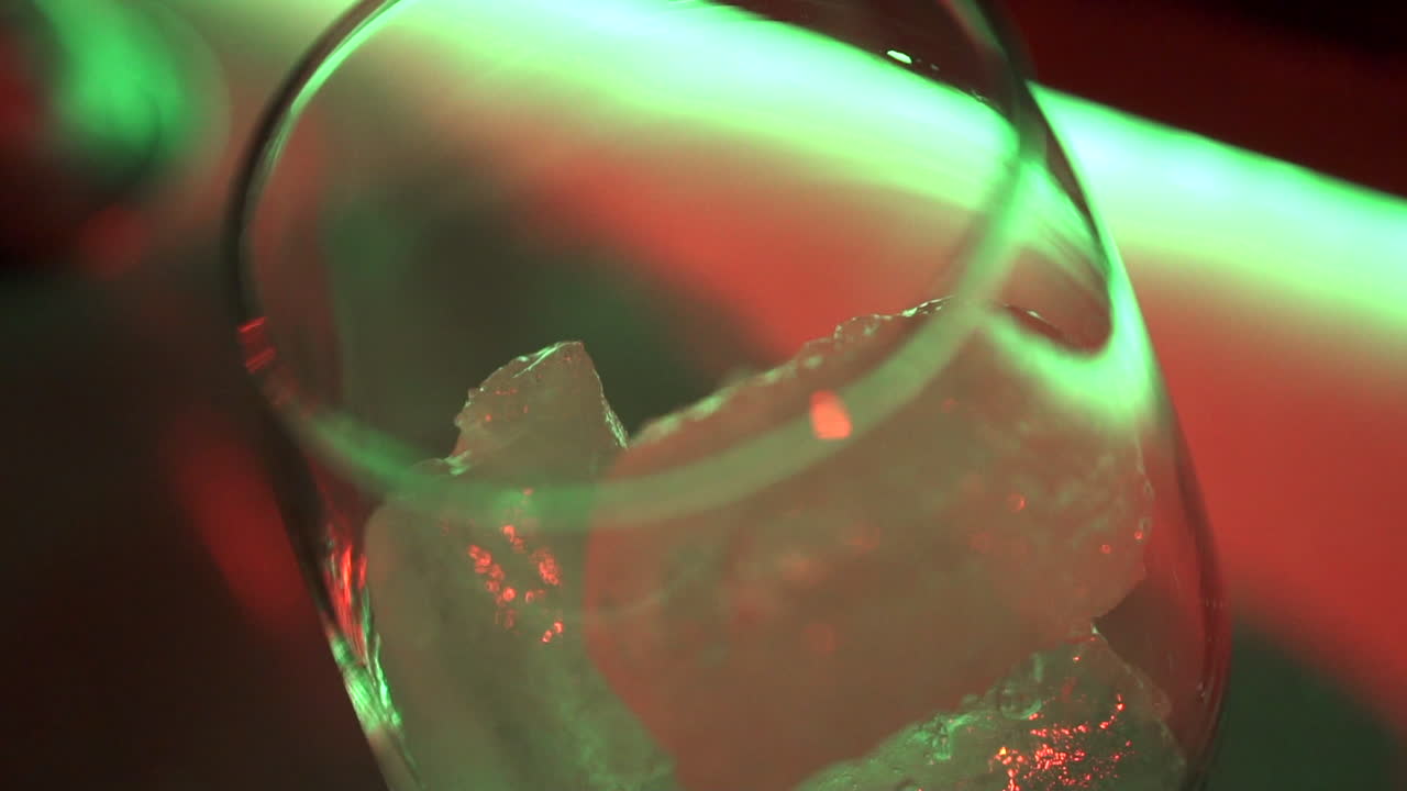 Vibrant cocktail with ice and garnish shines under colorful lights in festive setting