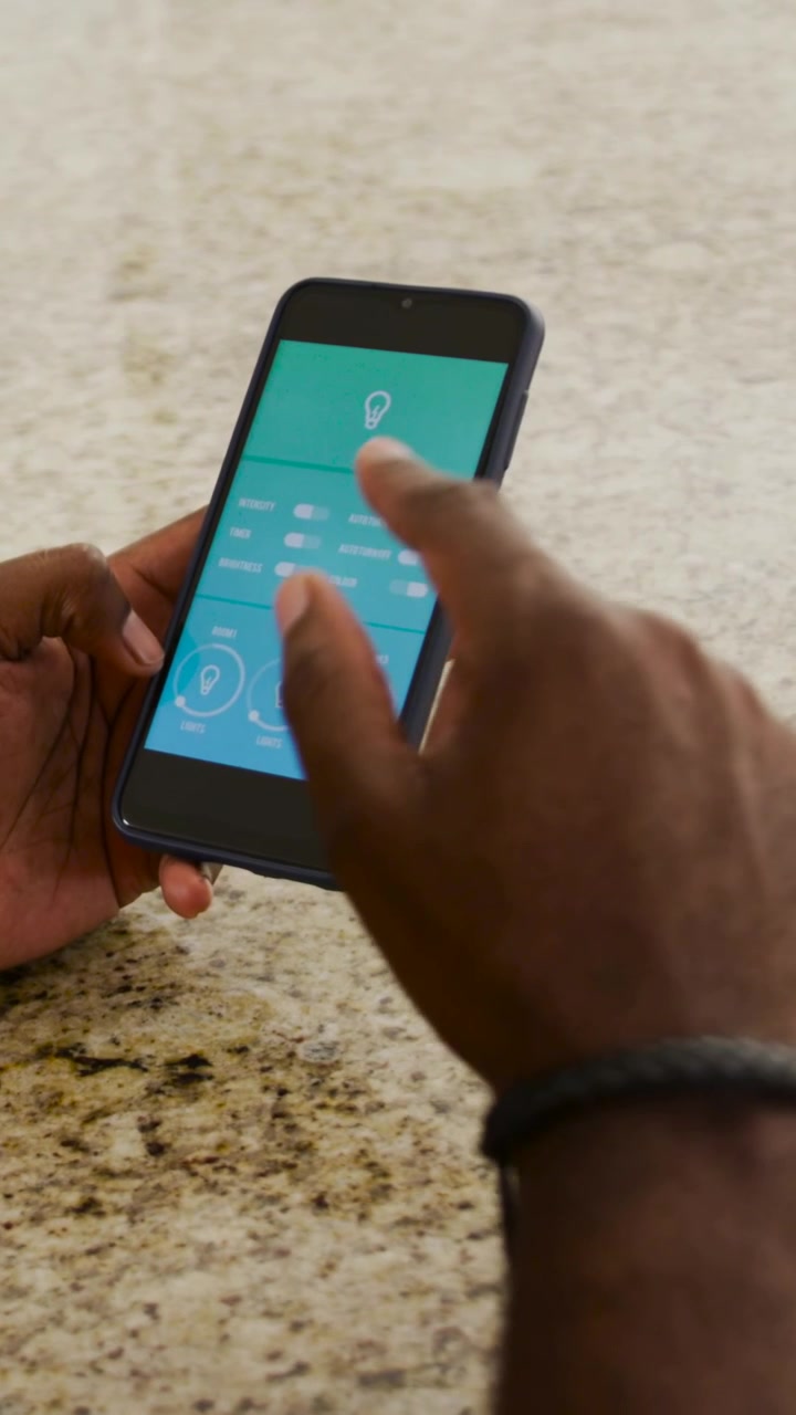 Vertical video: Using bulb app, man in yellow tapping controls, adjusting lights at kitchen counter
