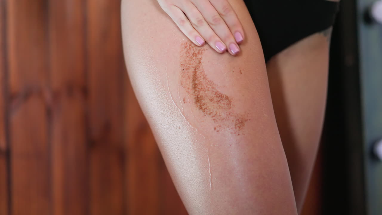 Giovane donna applica scrub al caffè sulla coscia massaggiando