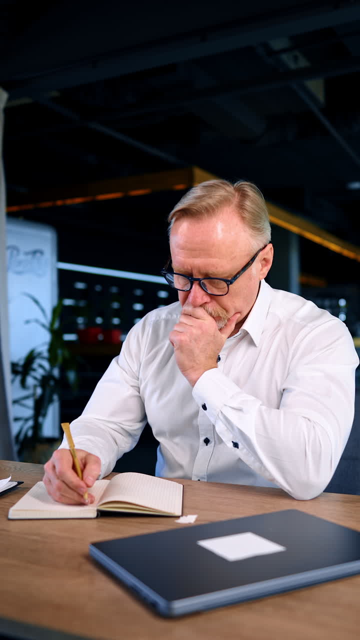 Productive multitasking businessman sitting at desk in office. Man taking notes, drinking coffee and feeling energetic. Vertical video.