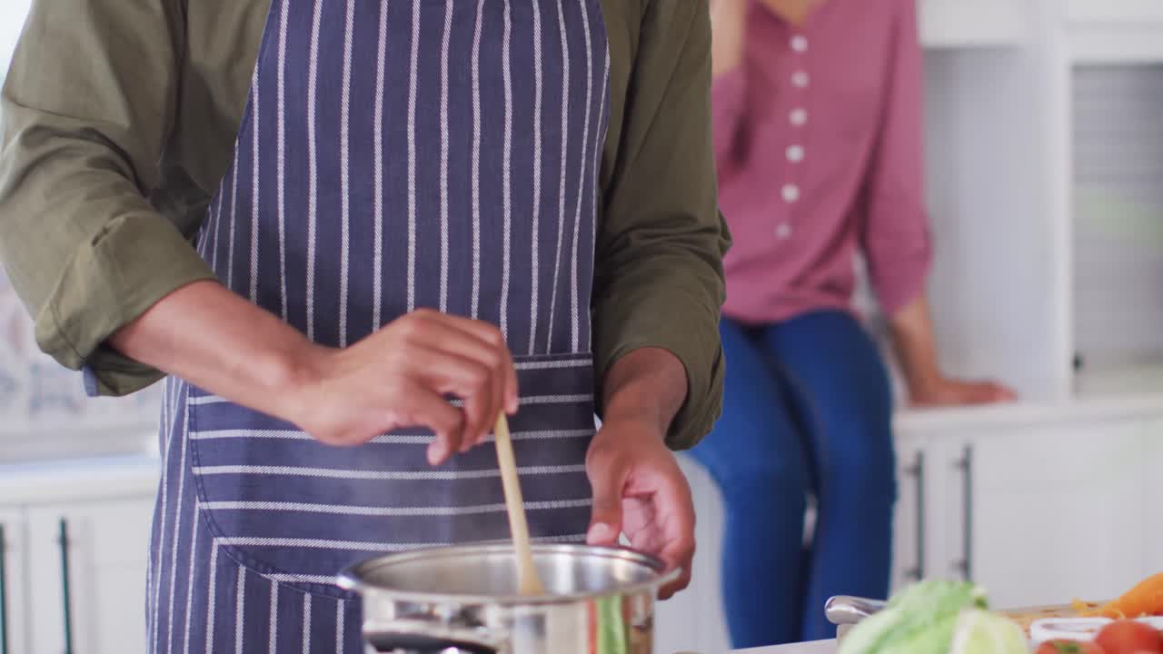 feliz pareja afroamericana cocinando y bebiendo vino en la cocina