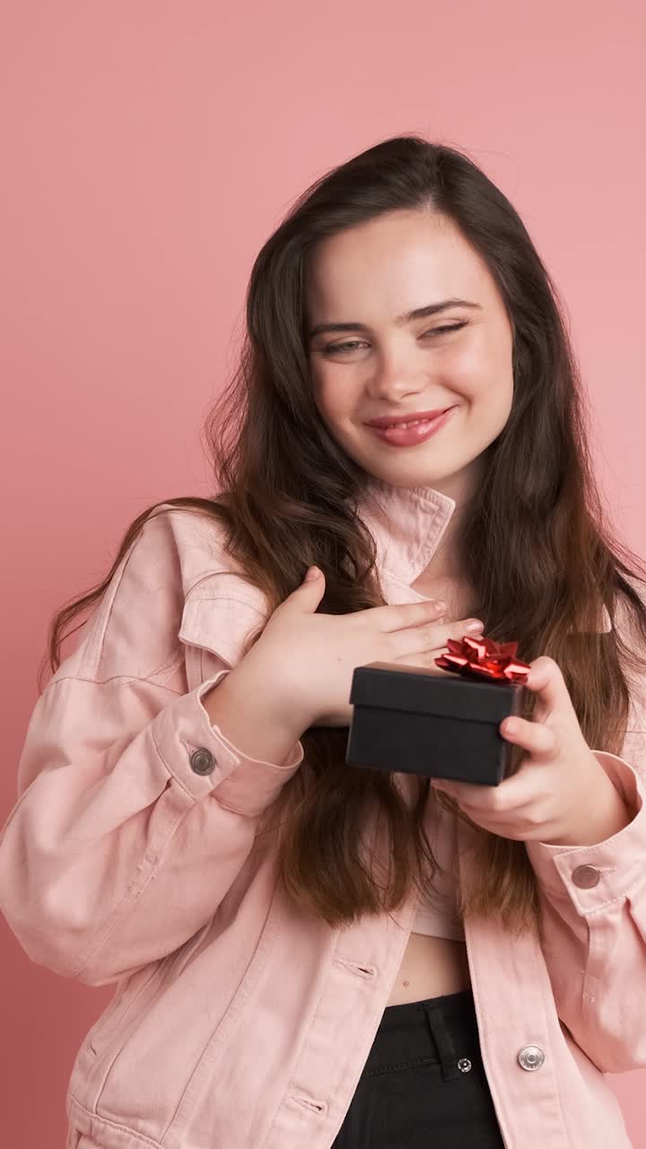 Happy young woman receiving gift box in pink studio