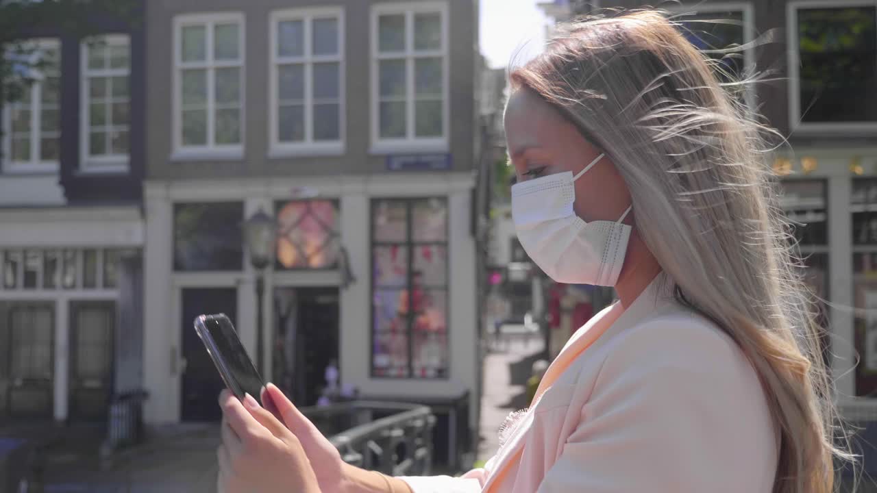 Tourist Woman Taking Selfie Using Her Cellphone Standing On Canal Bridge In Amsterdam, Netherlands During Covid-19 Outbreak