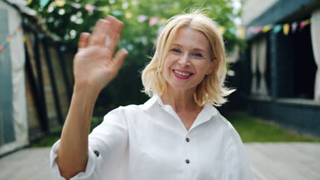 Smiling Woman Waving at Camera in Outdoor Setting