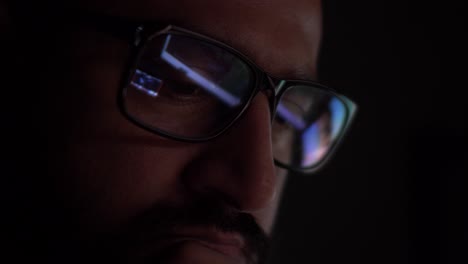 asian male with reflection of computer screens seen in glasses in dark room