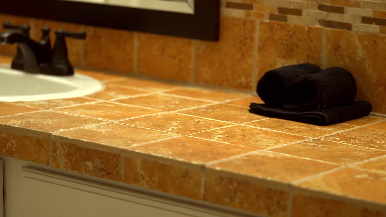 lavabos blancos en el baño con grifos de color marrón oscuro y encimera de mosaicos y placa para salpicaduras