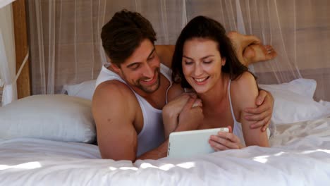 Glückliches-Paar,-Das-Ein-Digitales-Tablet-Nutzt,-Während-Es-Auf-Dem-Bett-Liegt-4K