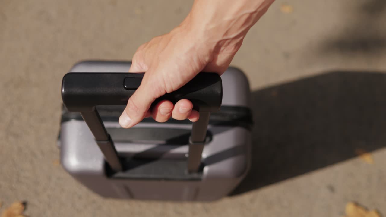 Person holder en grå trillekoffert