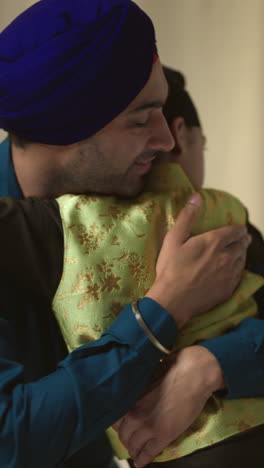 vertical video studio shot of loving sikh father embracing son both wearing turbans against plain background 1