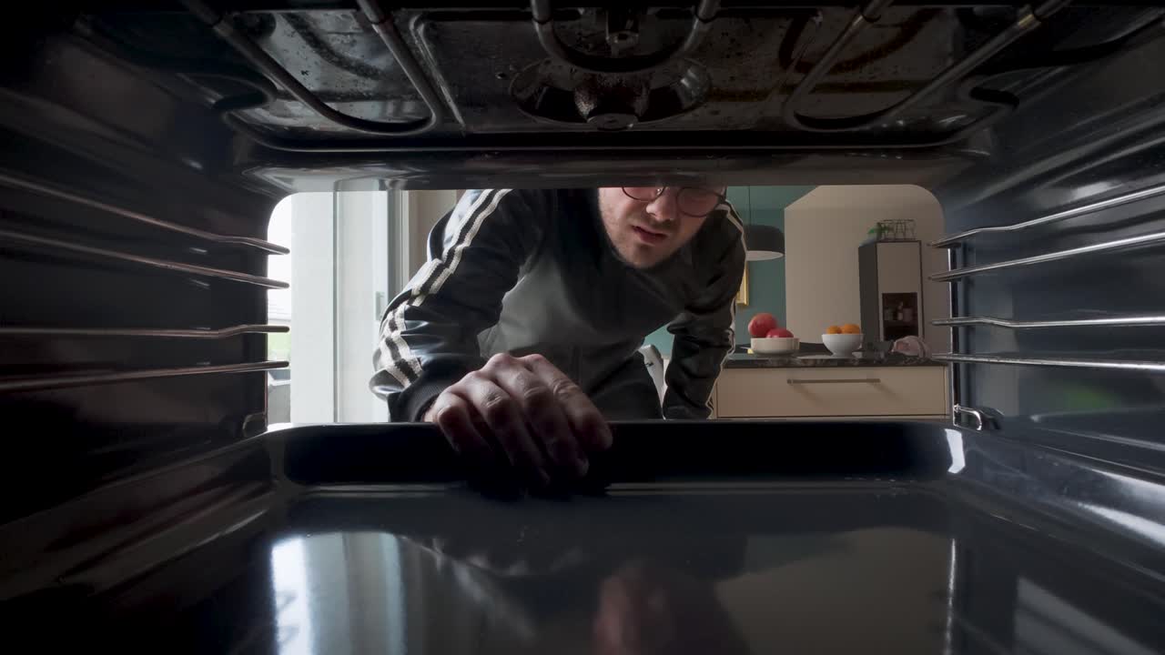 Point-of-view shot from inside an oven as a man places a baking tray inside. Ideal for cooking, home appliances, kitchen routines, or household lifestyle themes