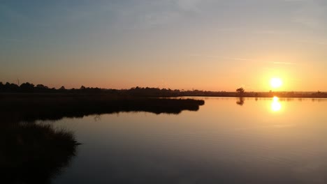 Luftausstoß-über-Wasser-Schöner-Sonnenuntergang-See-Silhouette-Blaugrüner-Orangefarbener-Himmel