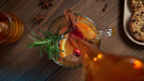 preparing warming winter tea with orange, cinnamon, rosemary and anise - table top view of the stream pouring to the cup