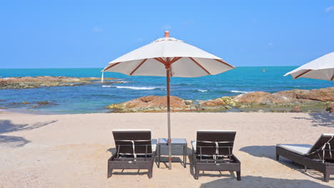 Seafront-Two-Sunbeds-Under-Umbrella-In-Tropical-Rocky-Beach-on-a-sunny-day