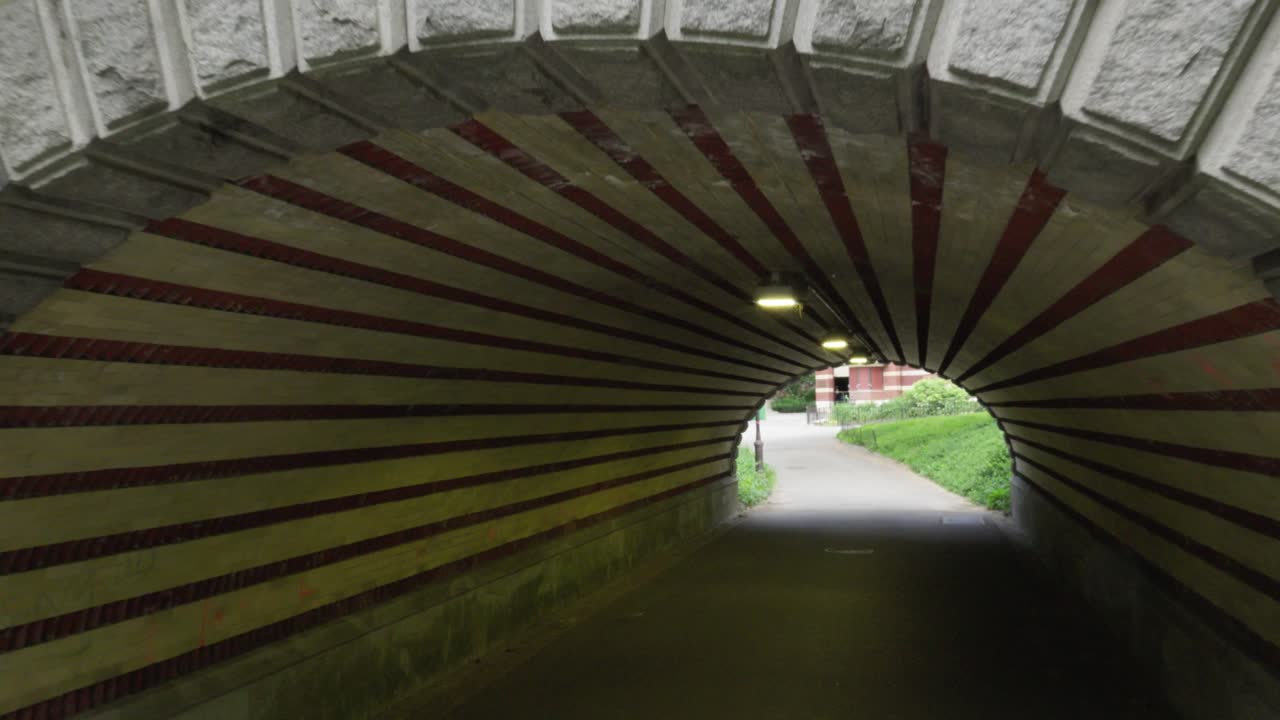 The camera enters a distinct white and red candy cane-striped underpass, a unique feature in New York City's Central Park