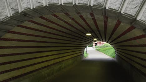 The camera enters a distinct white and red candy cane-striped underpass, a unique feature in New York City&#039;s Central Park