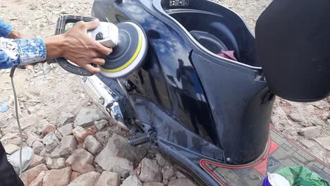 a man is rubbing polish the black motorcycle with a polisher at a workshop