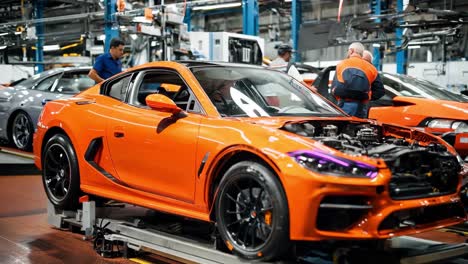 workers assemble a bright orange sports car in a manufacturing facility