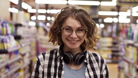 Portrait-young-woman-stands-in-front-of-the-camera-and-smiles-in-supermarket-feel-happy-girl-shopping-face-retail-store.-Pretty