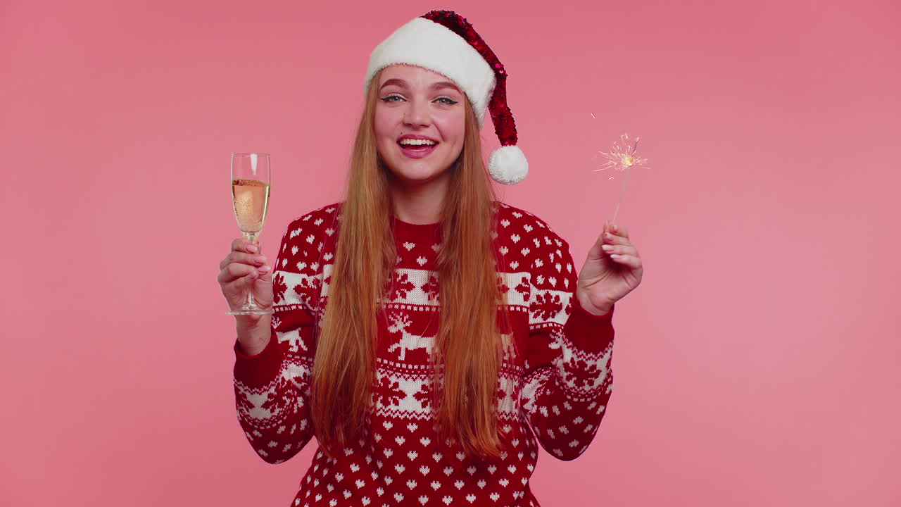 Lovely girl in Christmas Santa sweater dancing with bengal sparklers fireworks and champagne glass