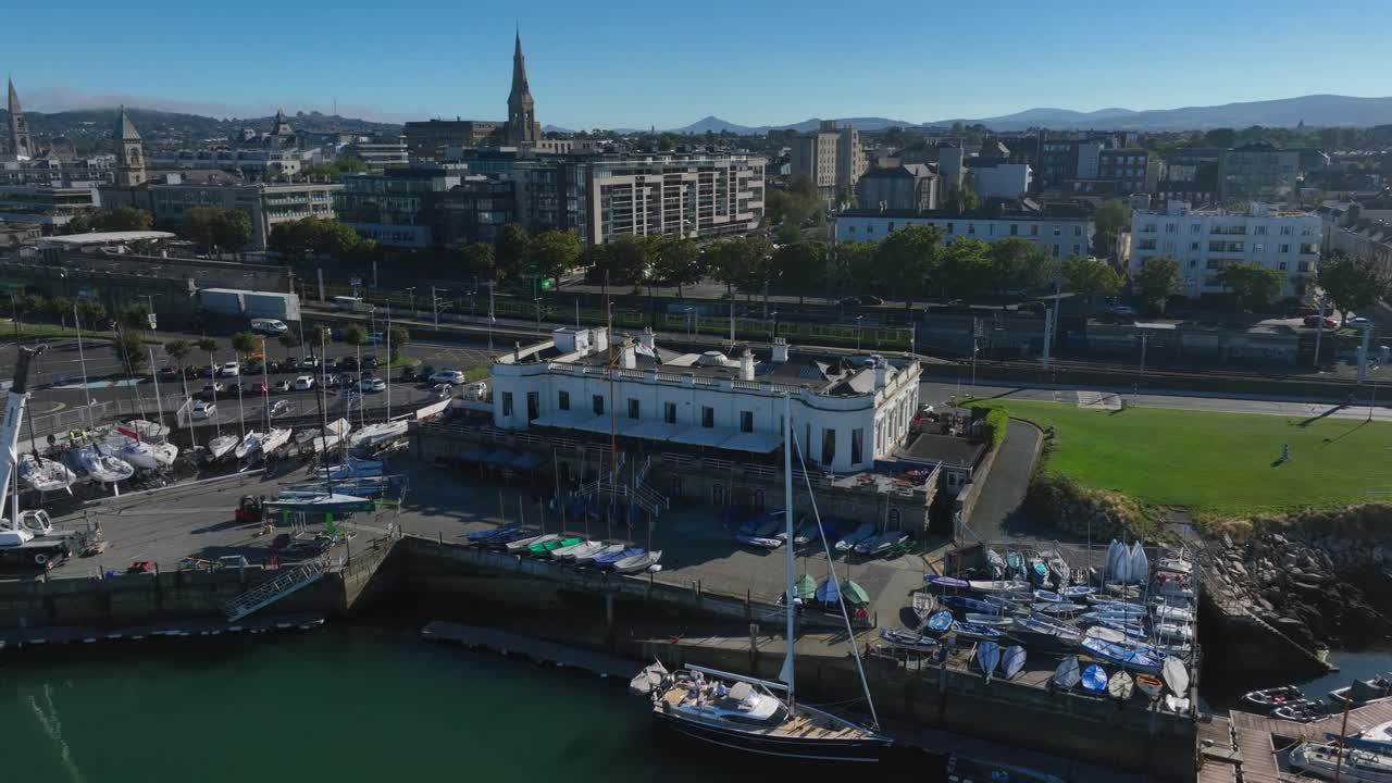 Royal Irish Yacht Club, Dún Laoghaire, County Dublin, Ireland, September 2024. Drone pulls away orbiting counter clockwise rising above yachts with Sandycove and Scotsman's Bay in the distance.