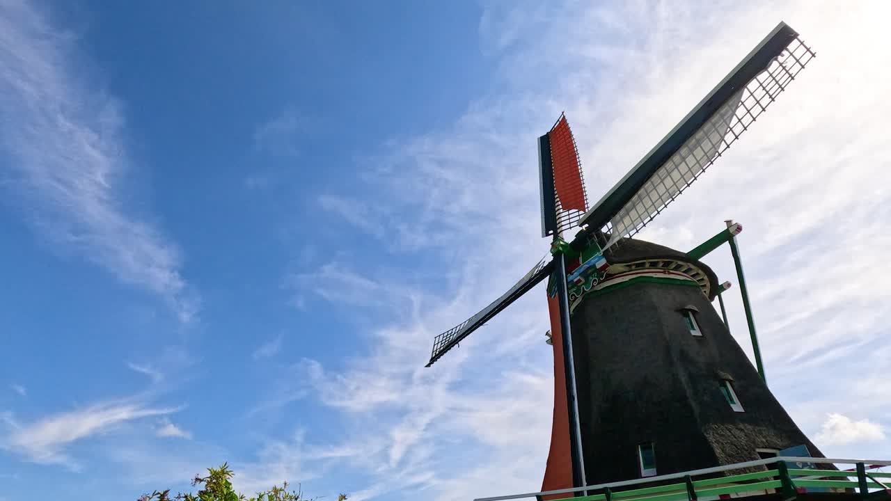 Historic windmill blades turning smoothly in daylight, low-angle view, vibrant summer sky, Zaandam